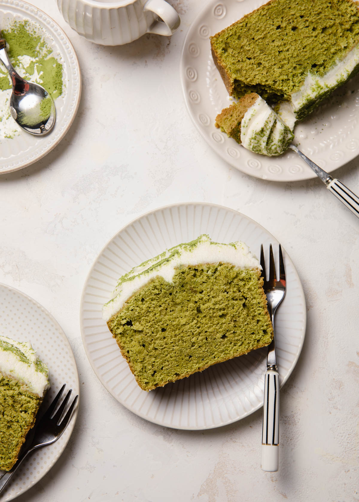 Slices of matcha cake on white plates with coconut frosting on top