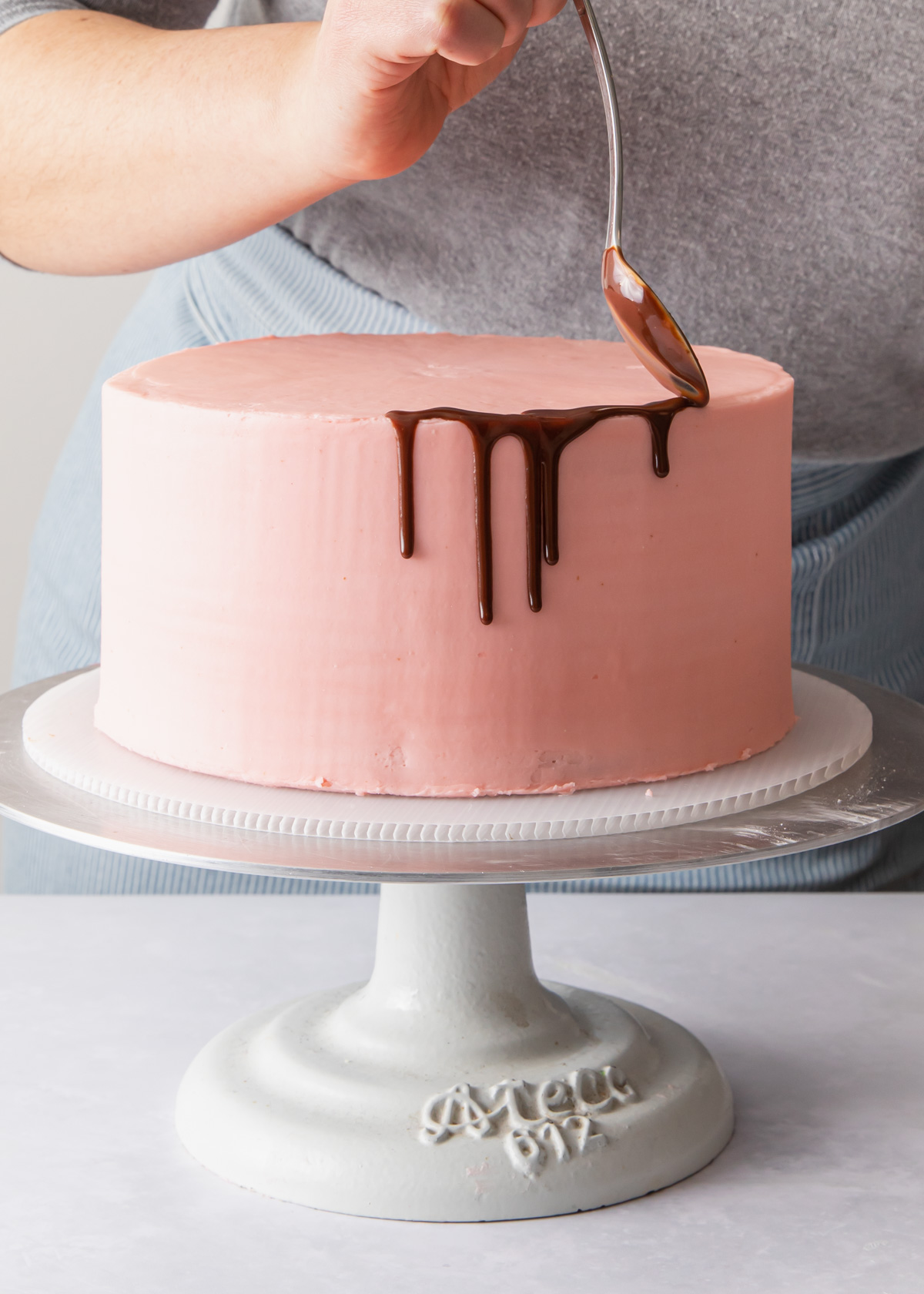 Dripping chocolate glaze on a pink cake with a spoon