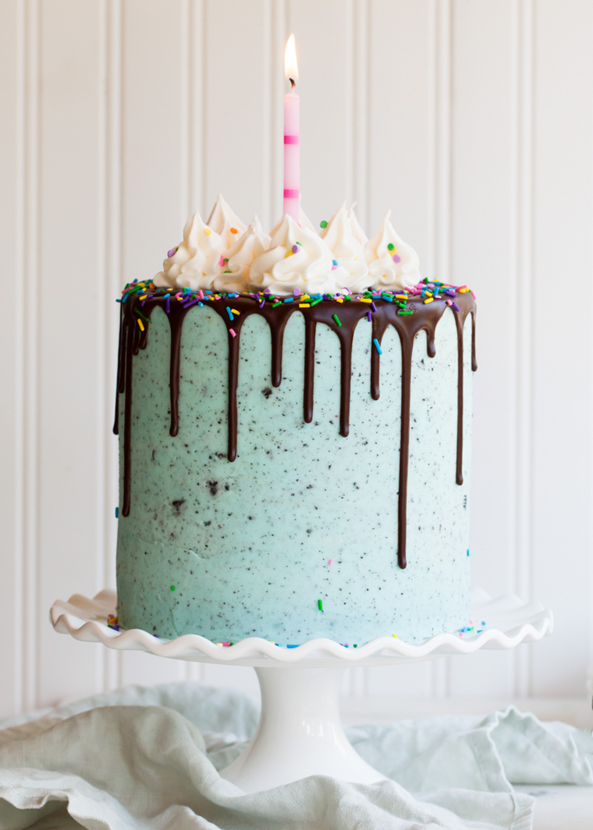 A side view of an Oreo layer cake with chocolate drips and piped buttercream frosting