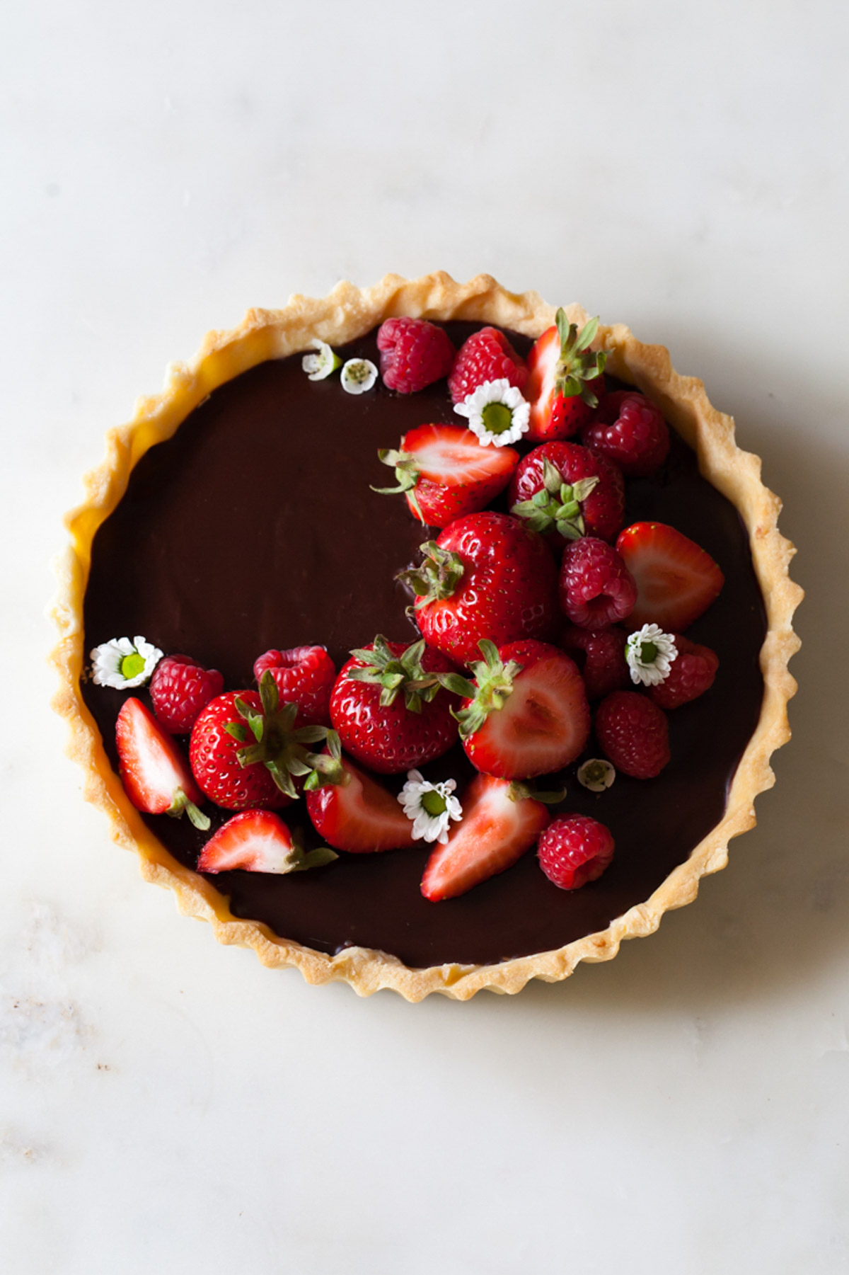 An overhead image of a classic chocolate ganache tart with fresh raspberries and strawberries on top
