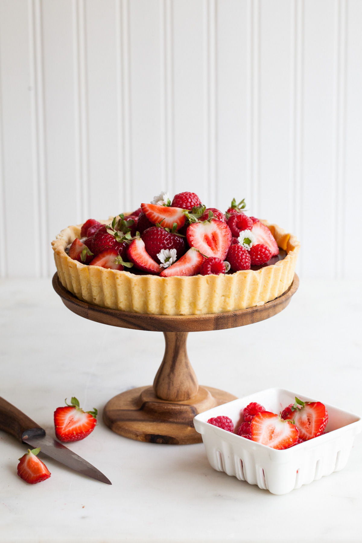 A chocolate ganache tart piled high with fresh berries on a cake stand