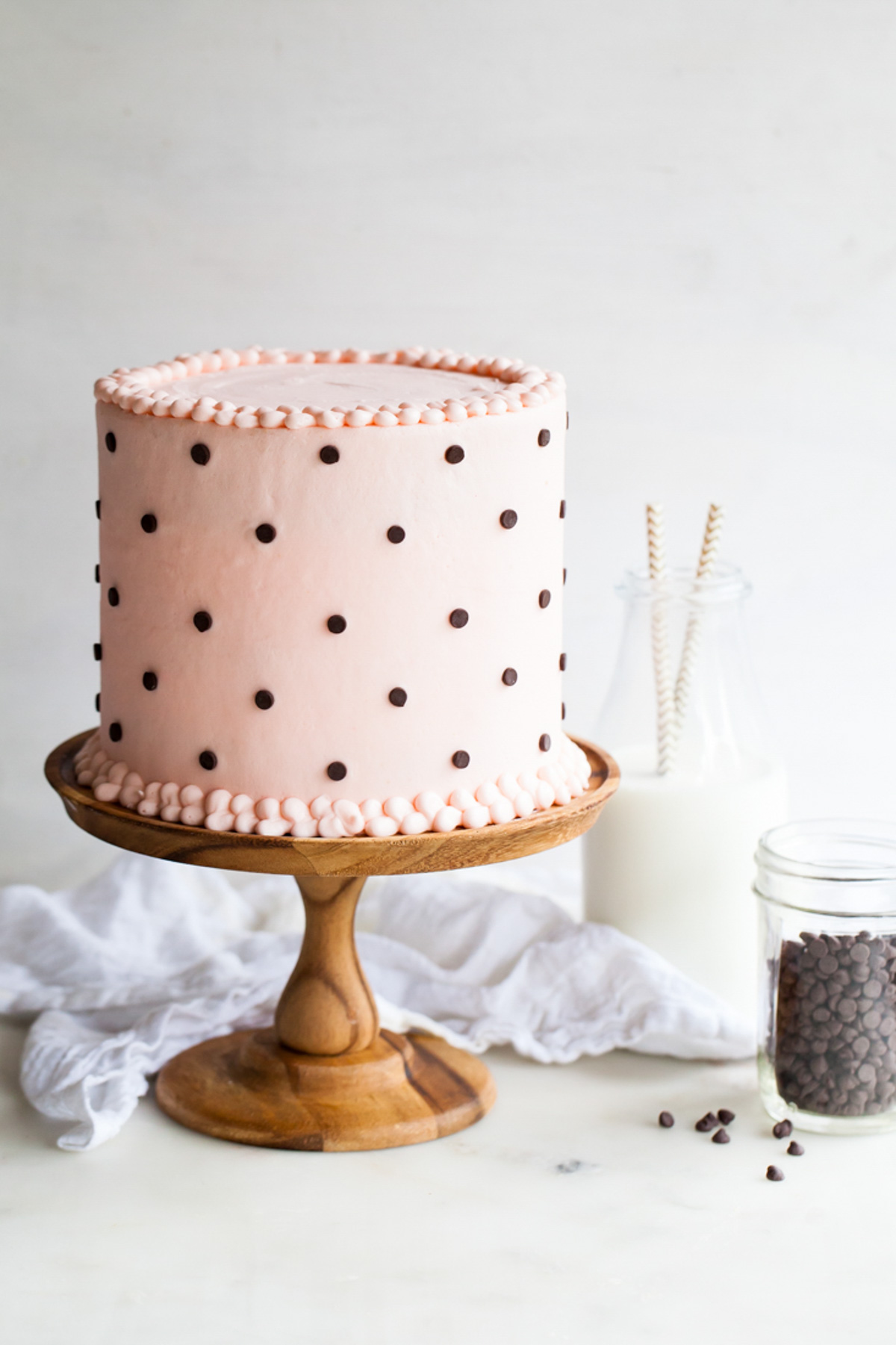Pink Milk and Cookies Cake with chocolate chip polka dots on a wooden cake stand.