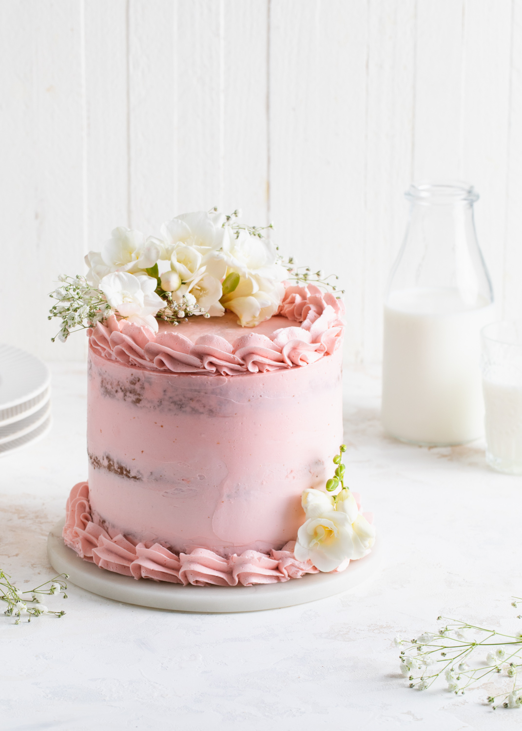 A pink, semi-naked layer cake with white flowers on top