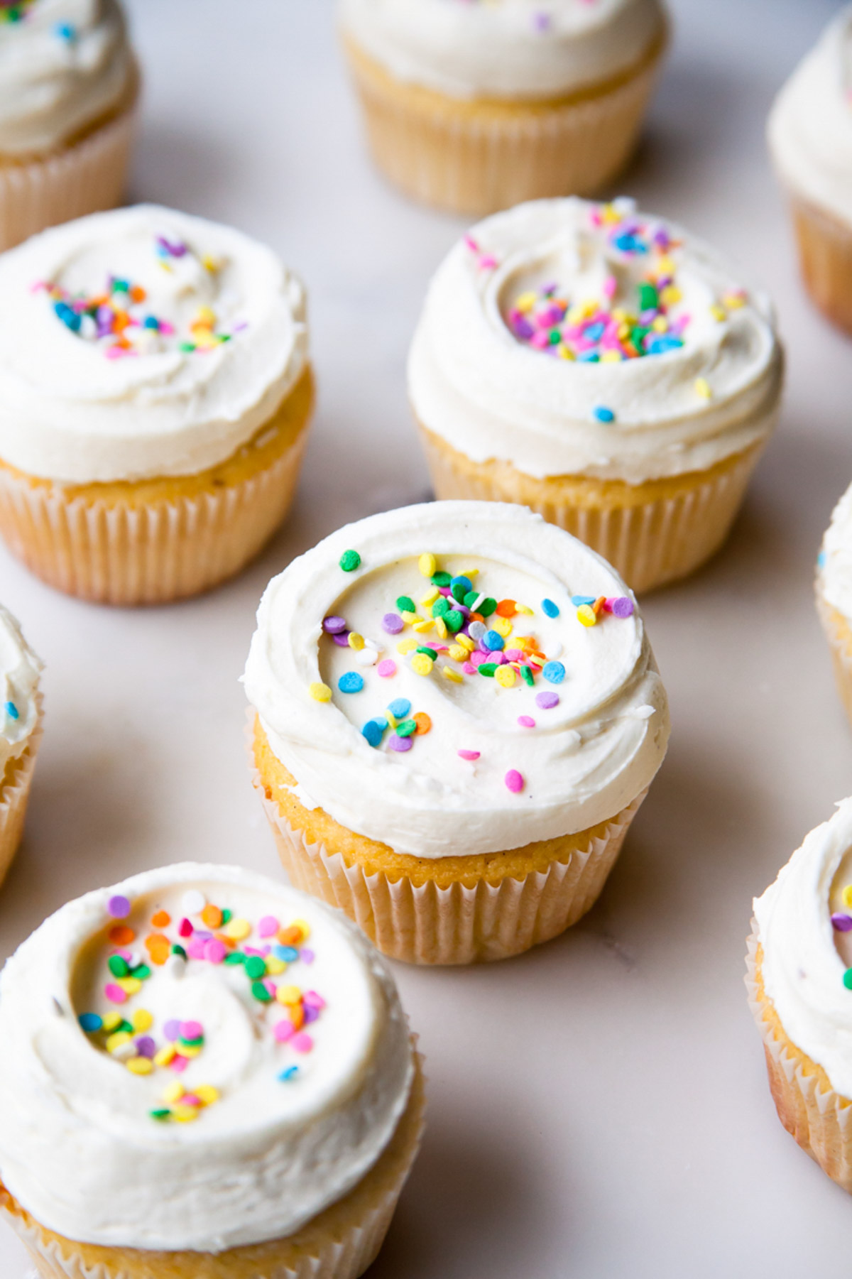 Vanilla cupcakes with perfect swirls on vanilla frosting and pastel sprinkles.
