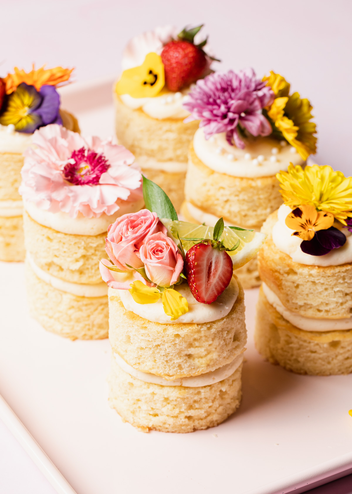 A pink tray with mini layer cakes on top that are decorated with fresh flowers