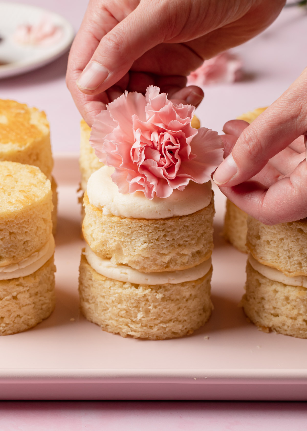Placing a pink flower on top of a mini vanilla cake