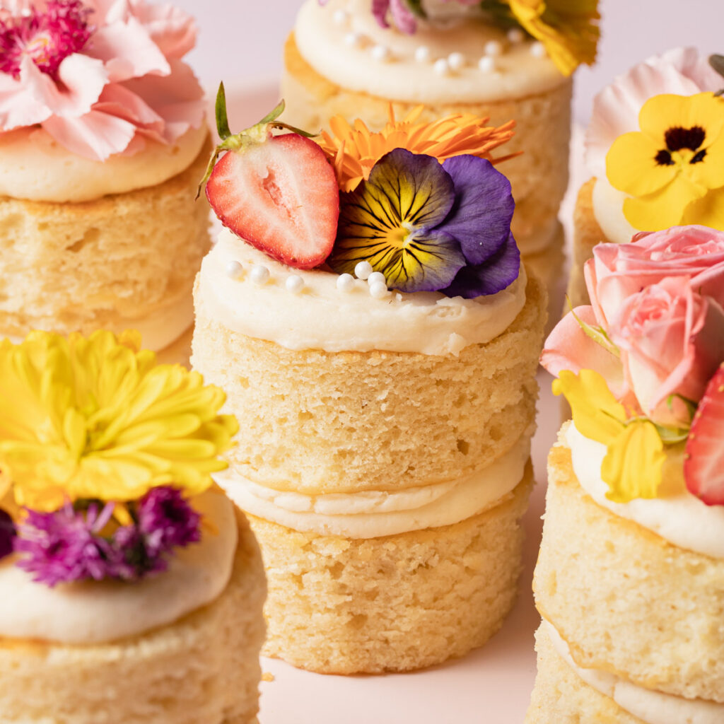 A bunch of mini two-layer vanilla cakes with flowers on top