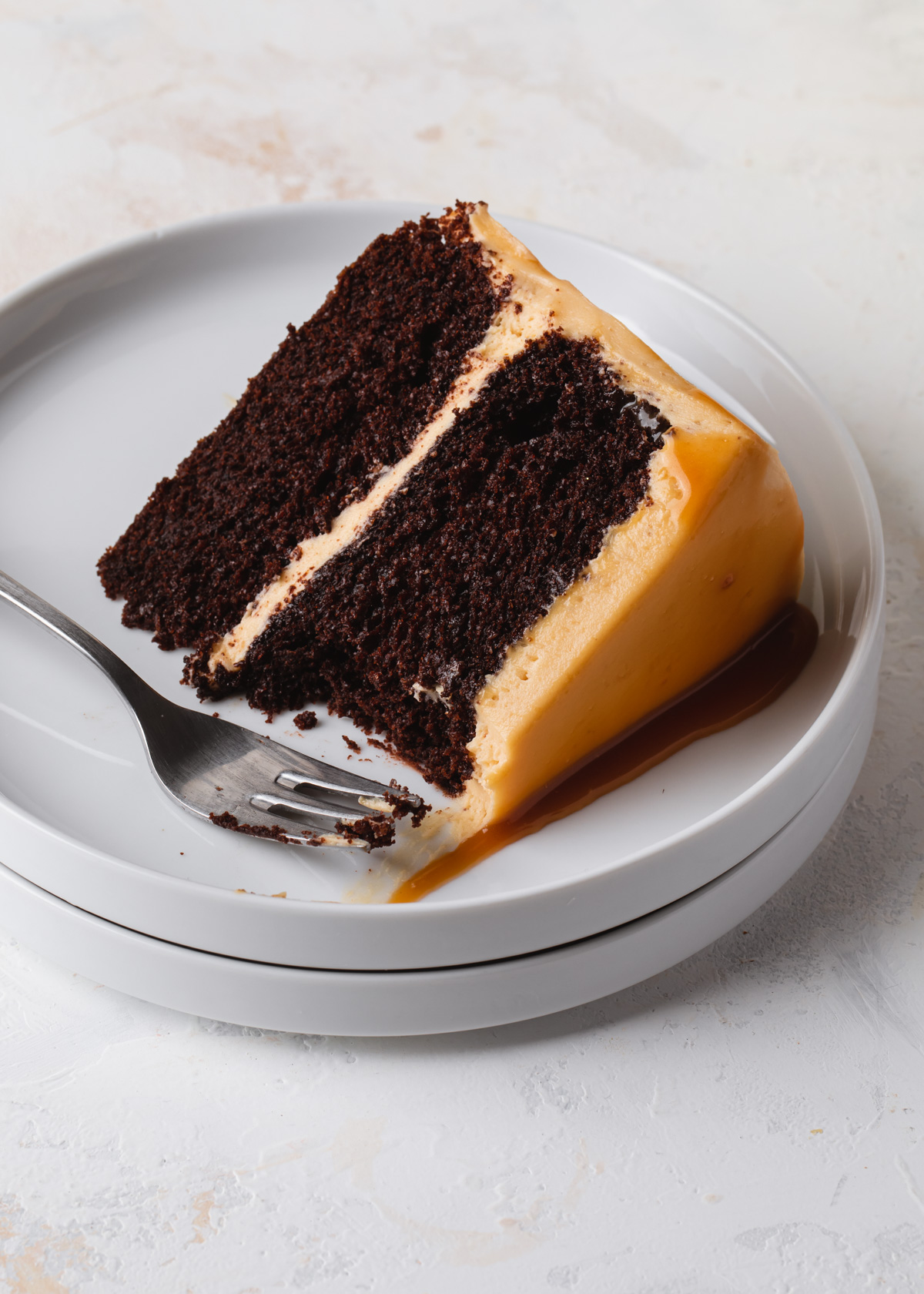 A close up of a slice of two-layer chocolate cake that's filled and frosted with caramel buttercream and a salted caramel sauce