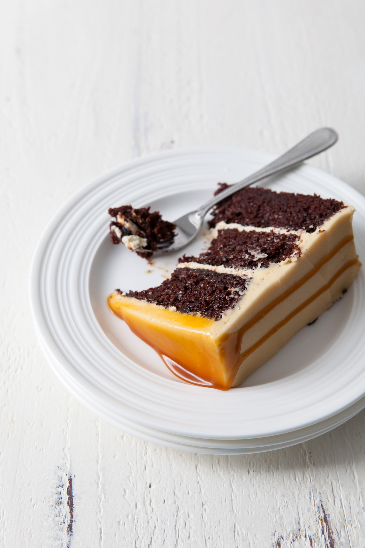 A slice of three layer chocolate cake with caramel frosting being eaten on a plate