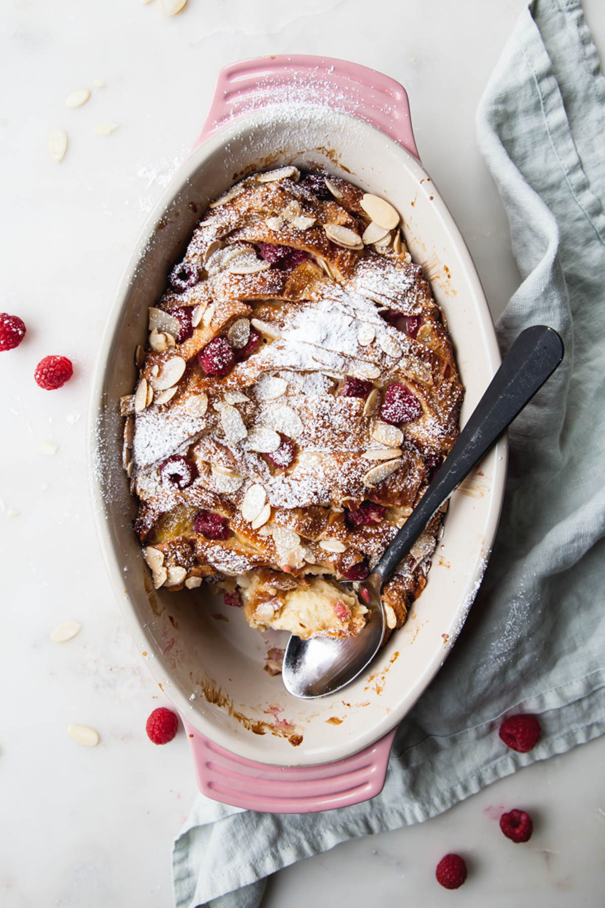 A dish of croissant bread pudding with raspberries and powdered sugar on top