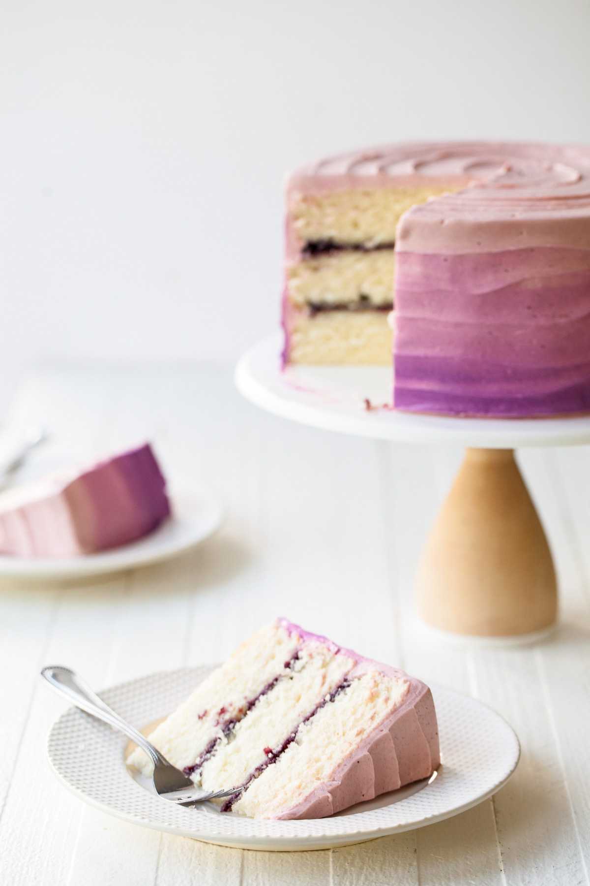 A sliced blueberry layer cake with three layers of fluffy white cake and blueberry jam filling.