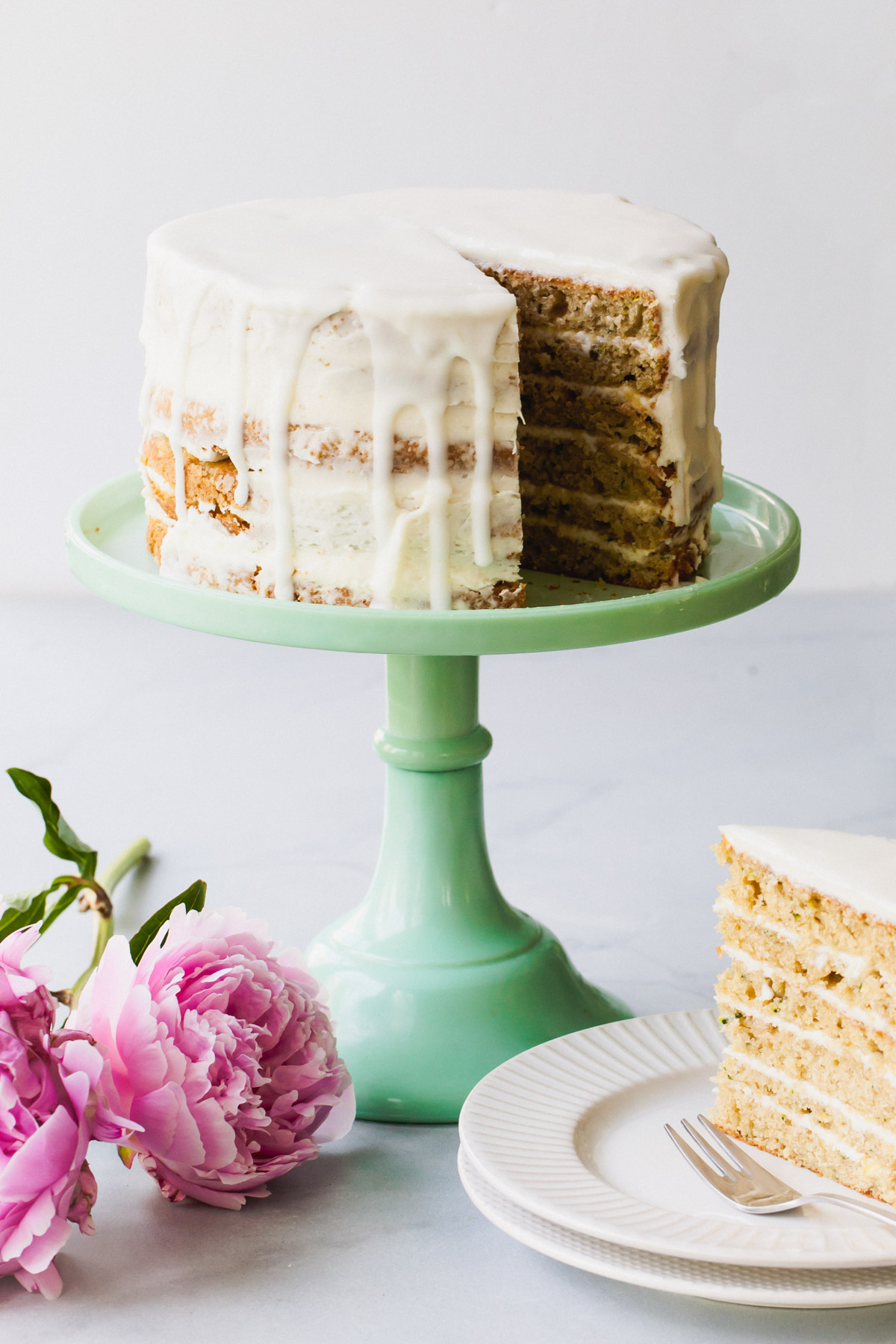 Lemon zucchini cake with goat cheese frosting on a green cake stand with a slice removed