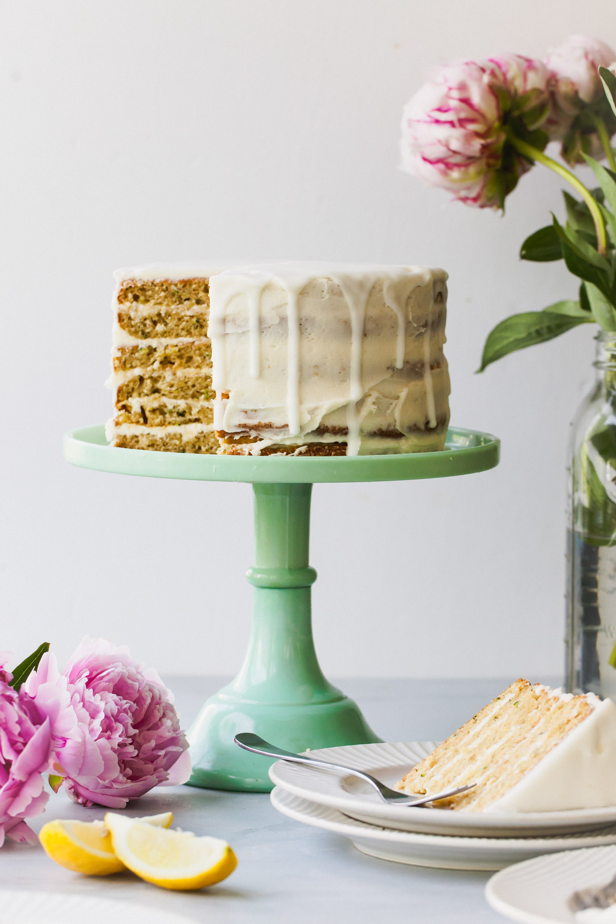 Lemon zucchini cake with goat cheese frosting on a green cake stand with a slice removed