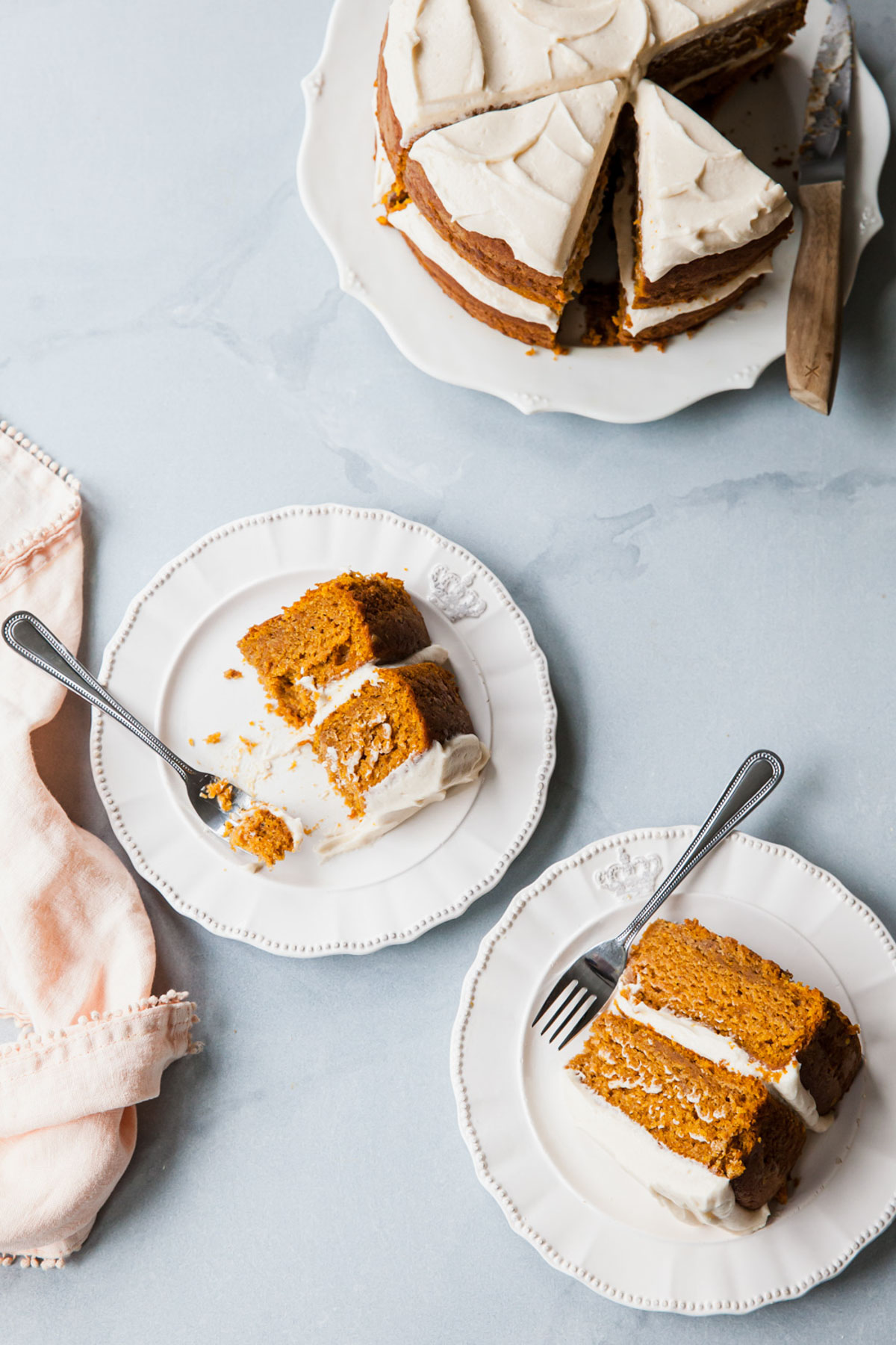 slices of pumpkin cake with cream cheese frosting on white plates