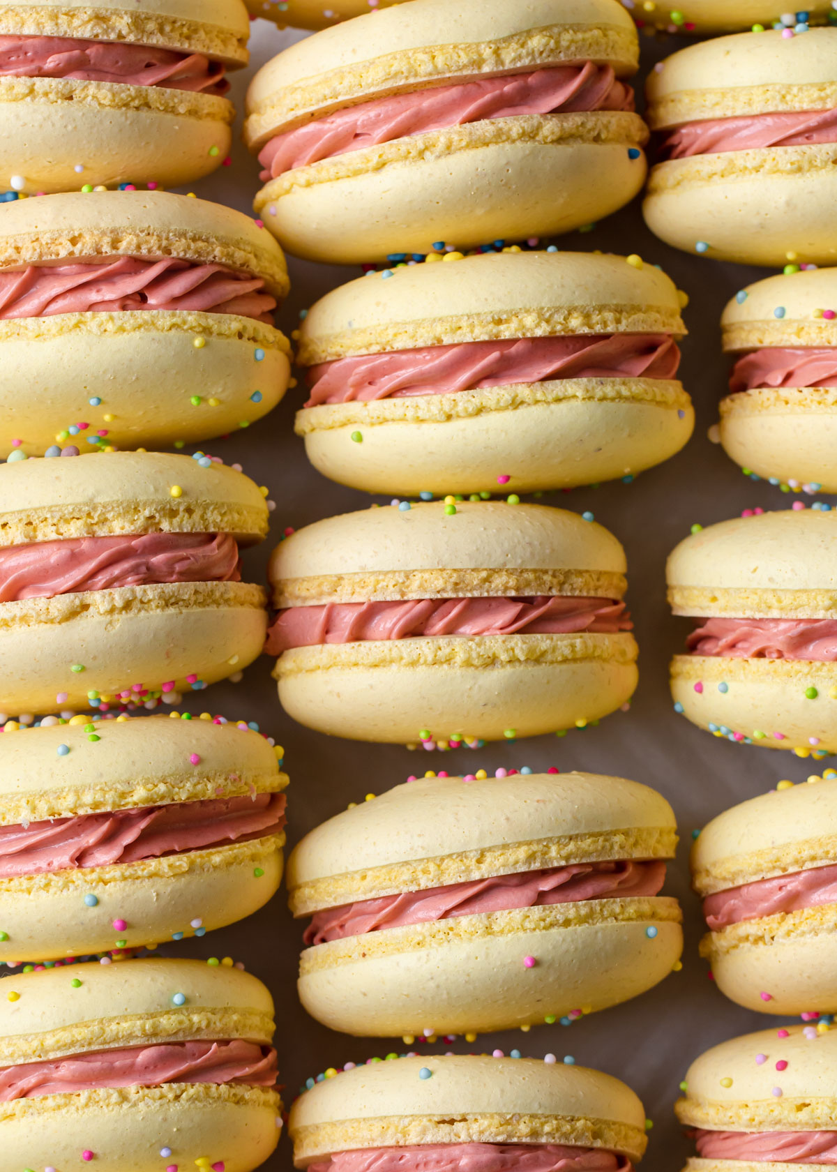 A close up of Yellow macarons with sprinkles and pink filling
