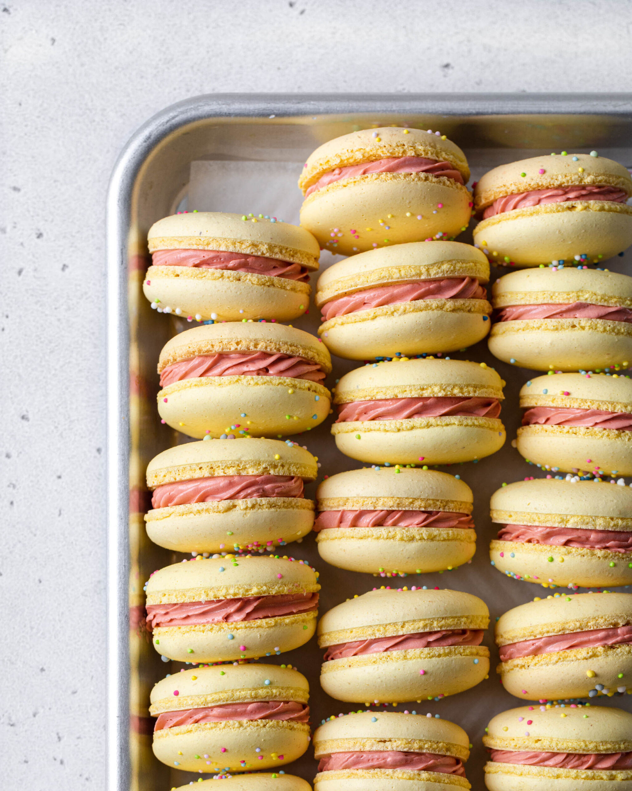 A tray of Yellow macarons with sprinkles and pink filling