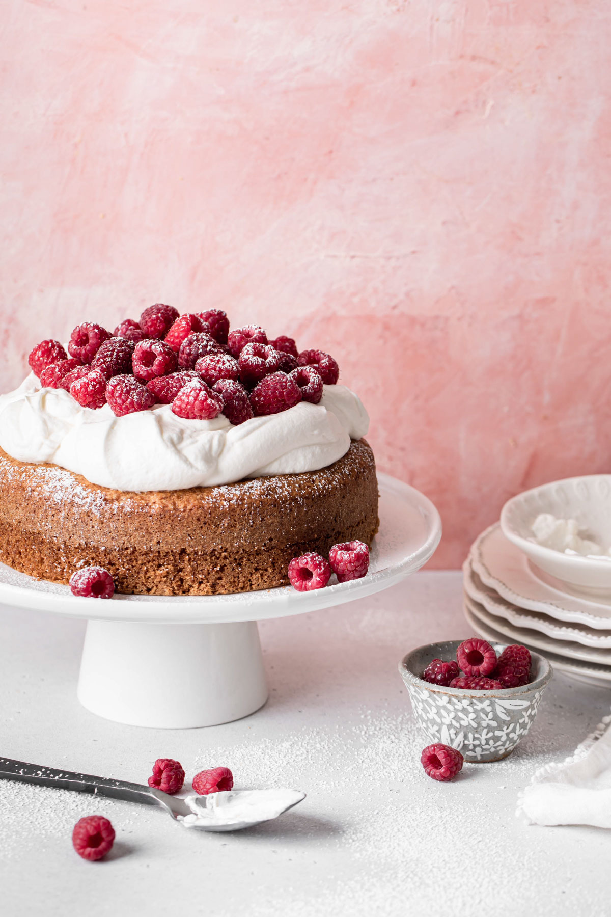 A single layer Greek yogurt cake with olive oil topped with whipped cream and tons of raspberries