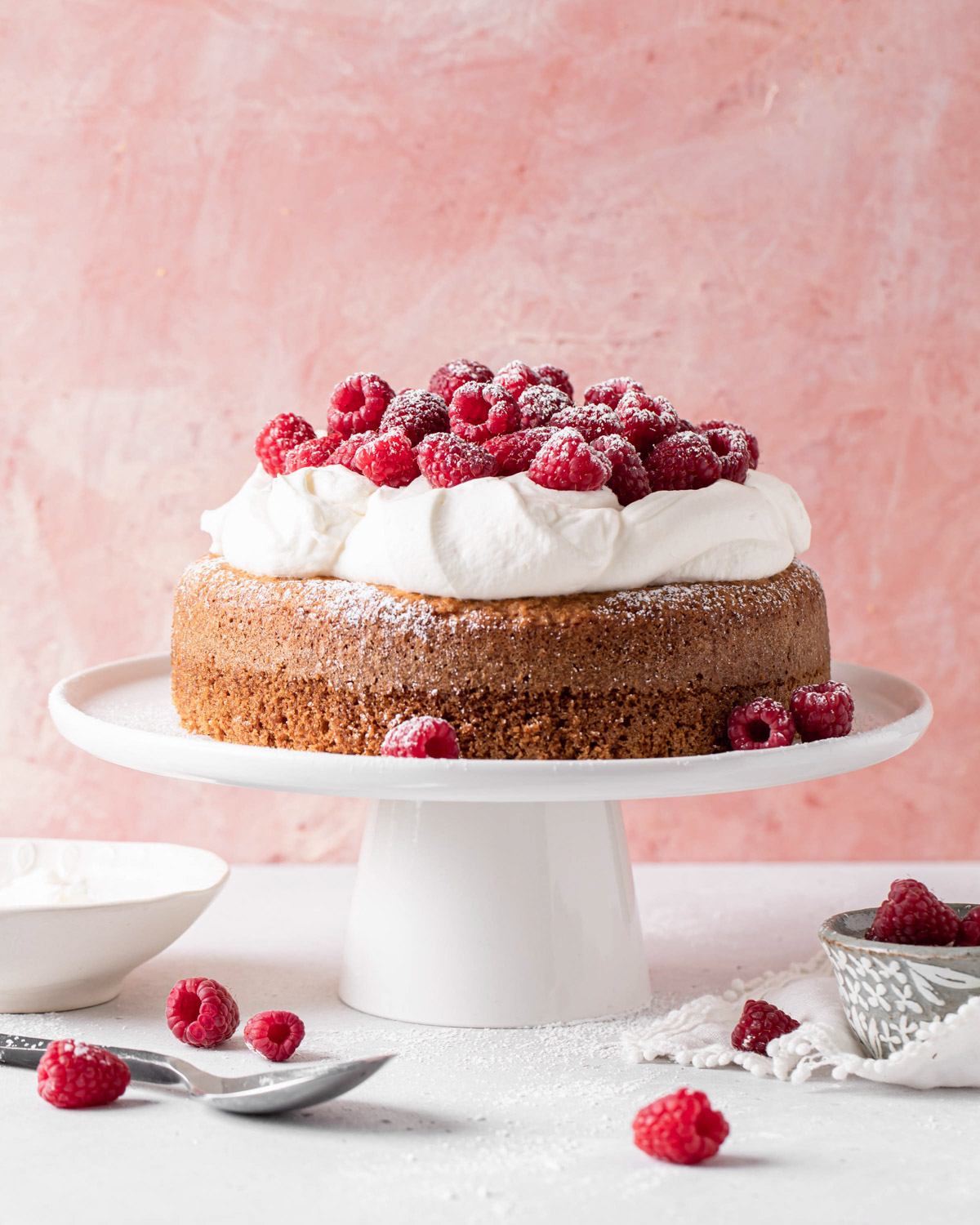 A single layer Greek yogurt cake with olive oil topped with whipped cream and tons of raspberries