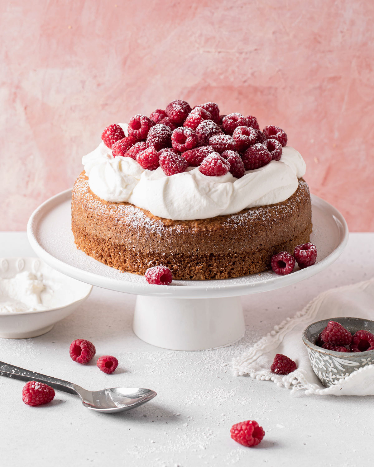 A single layer Greek yogurt cake with olive oil topped with whipped cream and tons of raspberries