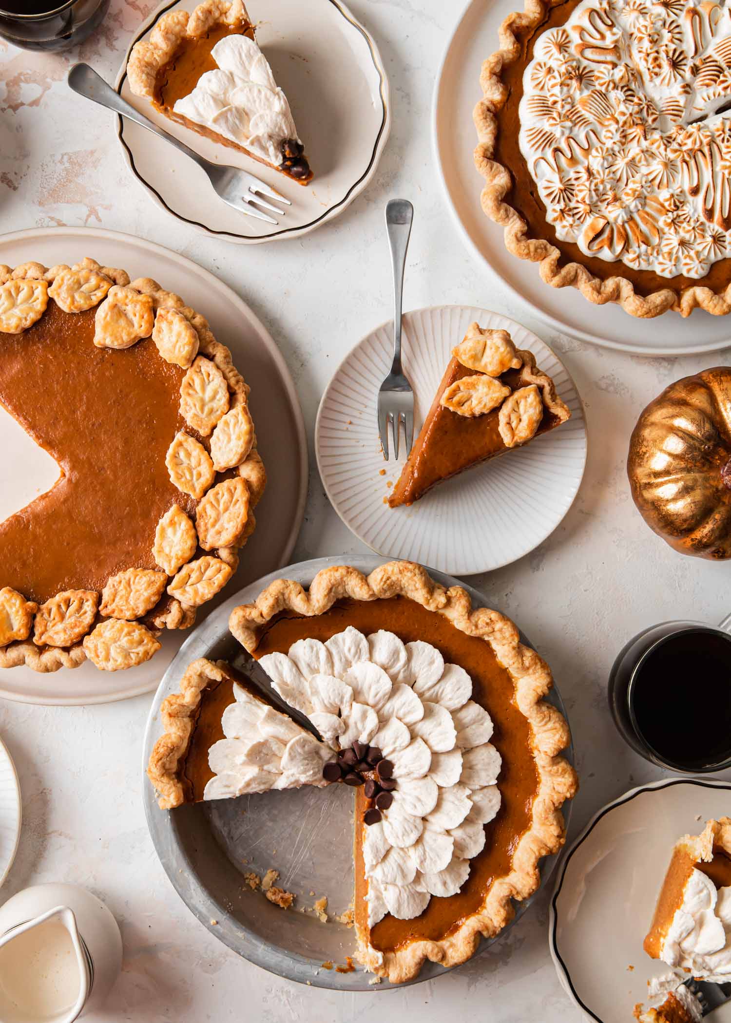 A table full of pumpkin pies and slices of pie that have been decorated three different ways