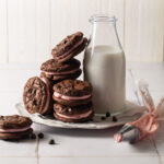 A plate of chocolate peppermint sandwich cookies with a bottle of milk