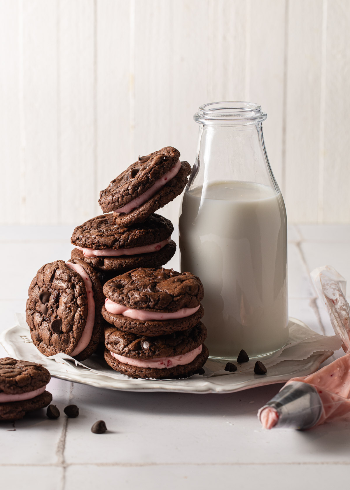 A plate of chocolate peppermint sandwich cookies with a bottle of milk