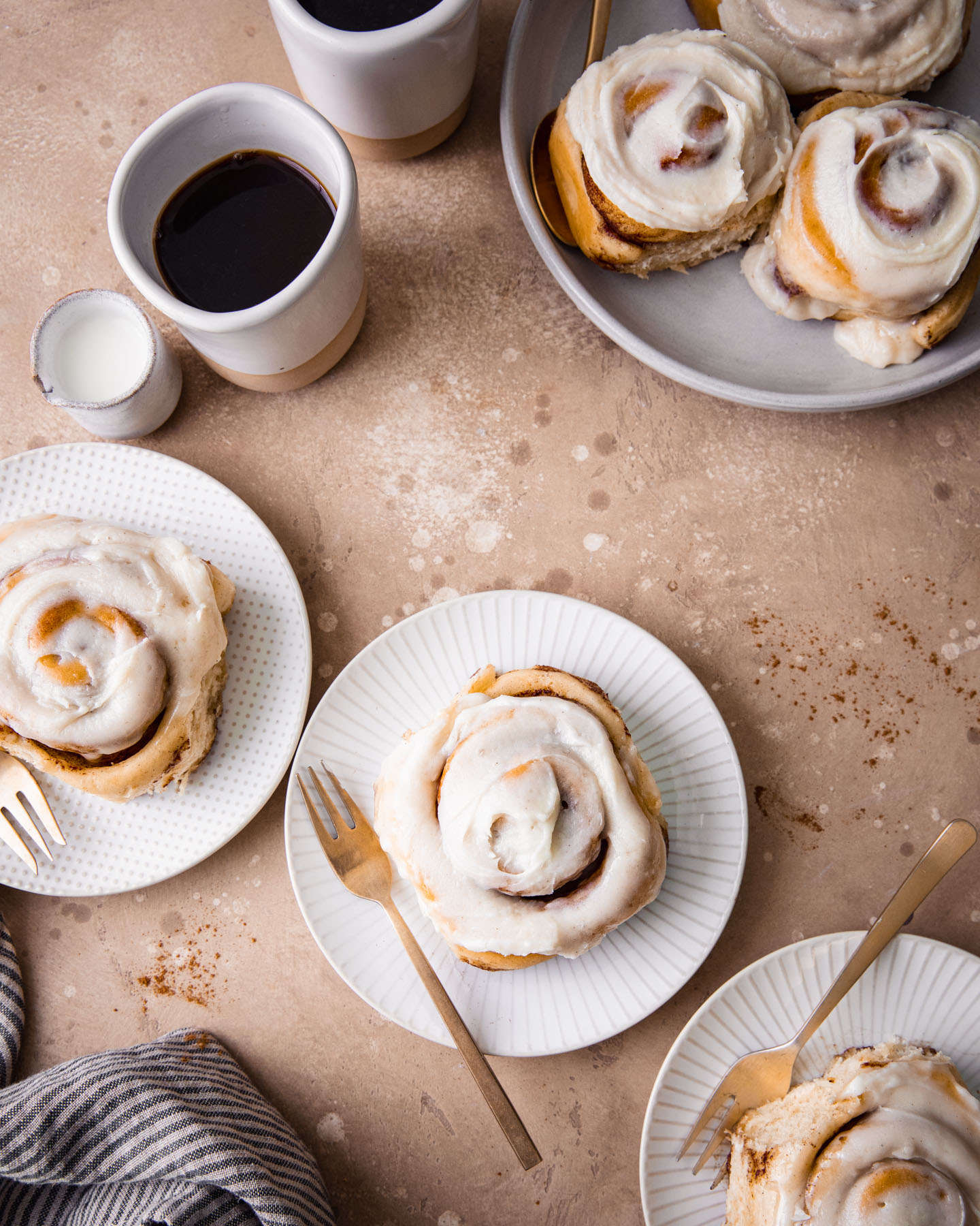 Iced cinnamon rolls on plates served with coffee