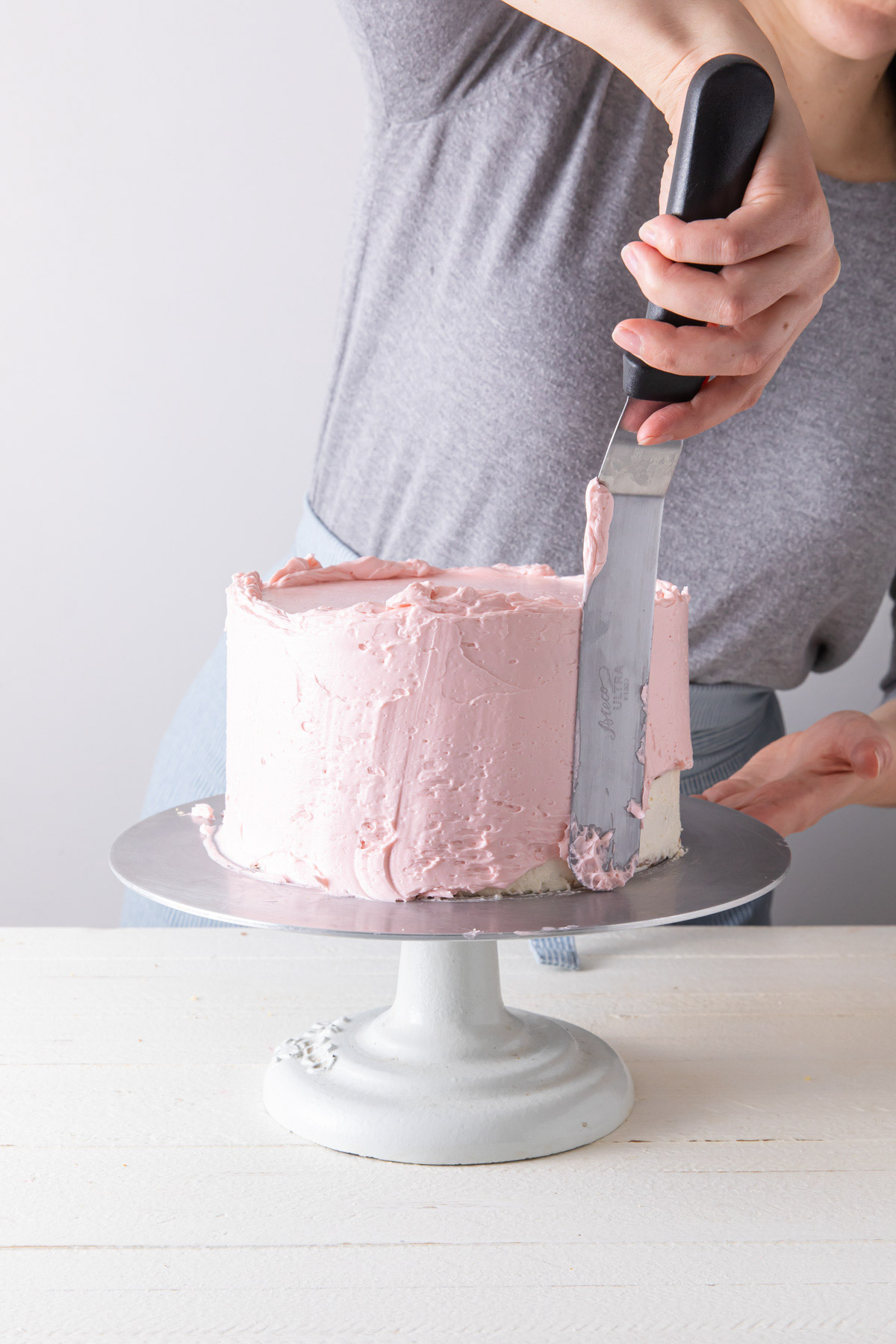 Frosting the sides of a layer cake with pink buttercream