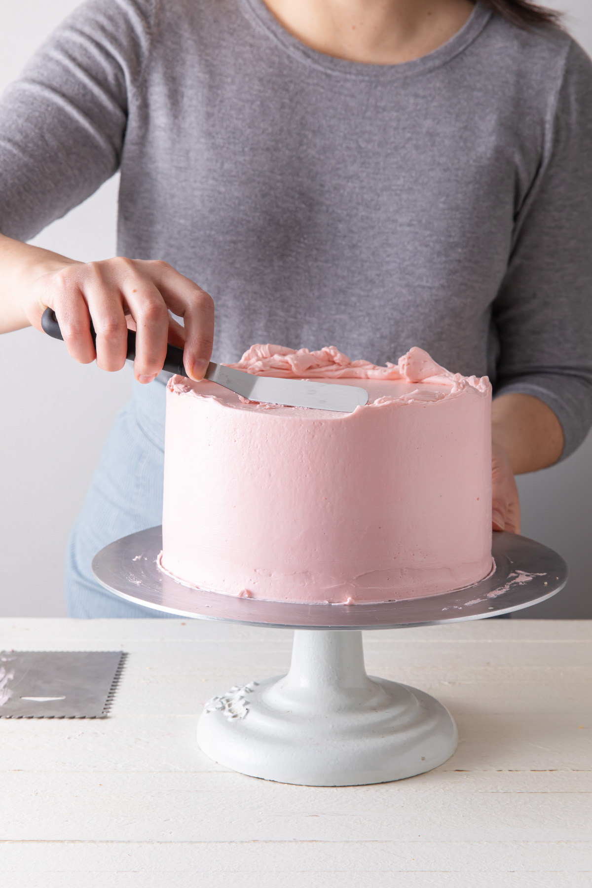 Frosting a cake with pink buttercream and an offset spatula