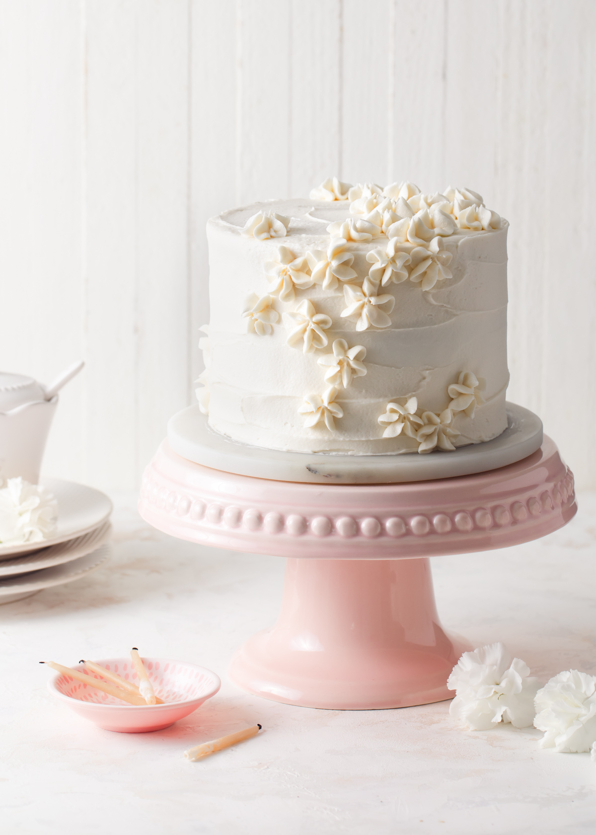 A 6-inch vanilla layer cake with piped vanilla frosting on a pink cake stand.