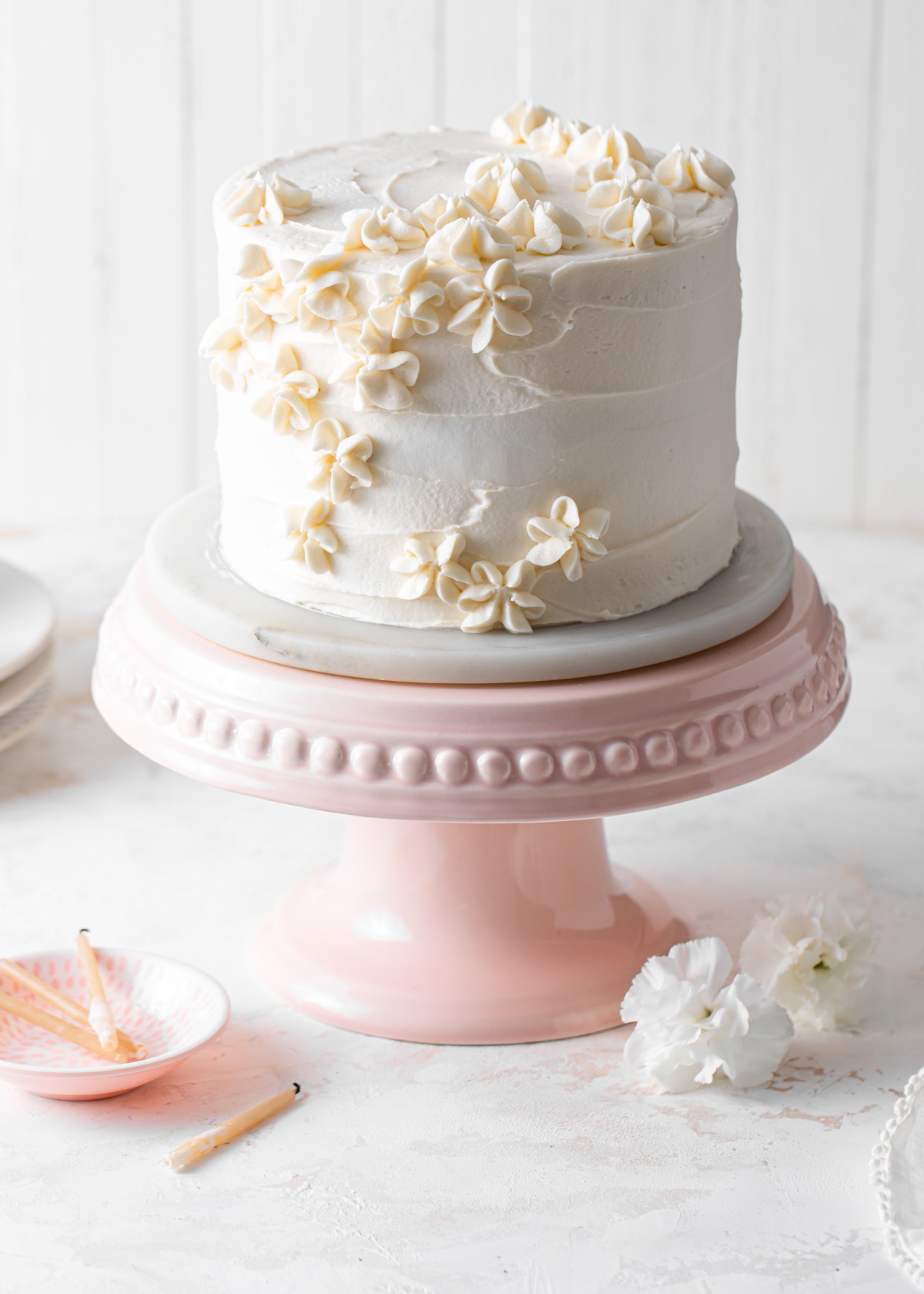 A 6-inch vanilla layer cake with piped vanilla frosting on a pink cake stand.