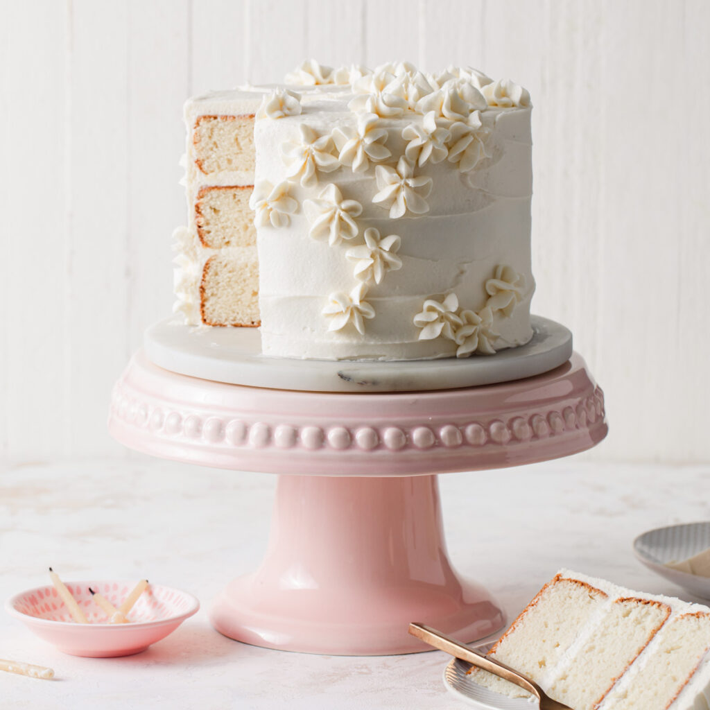 A three-layer vanilla cake with vanilla frosting on a pink cake stand