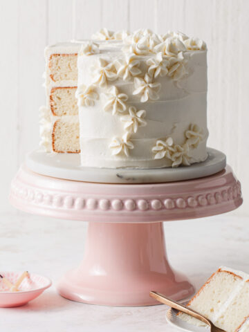 A three-layer vanilla cake with vanilla frosting on a pink cake stand