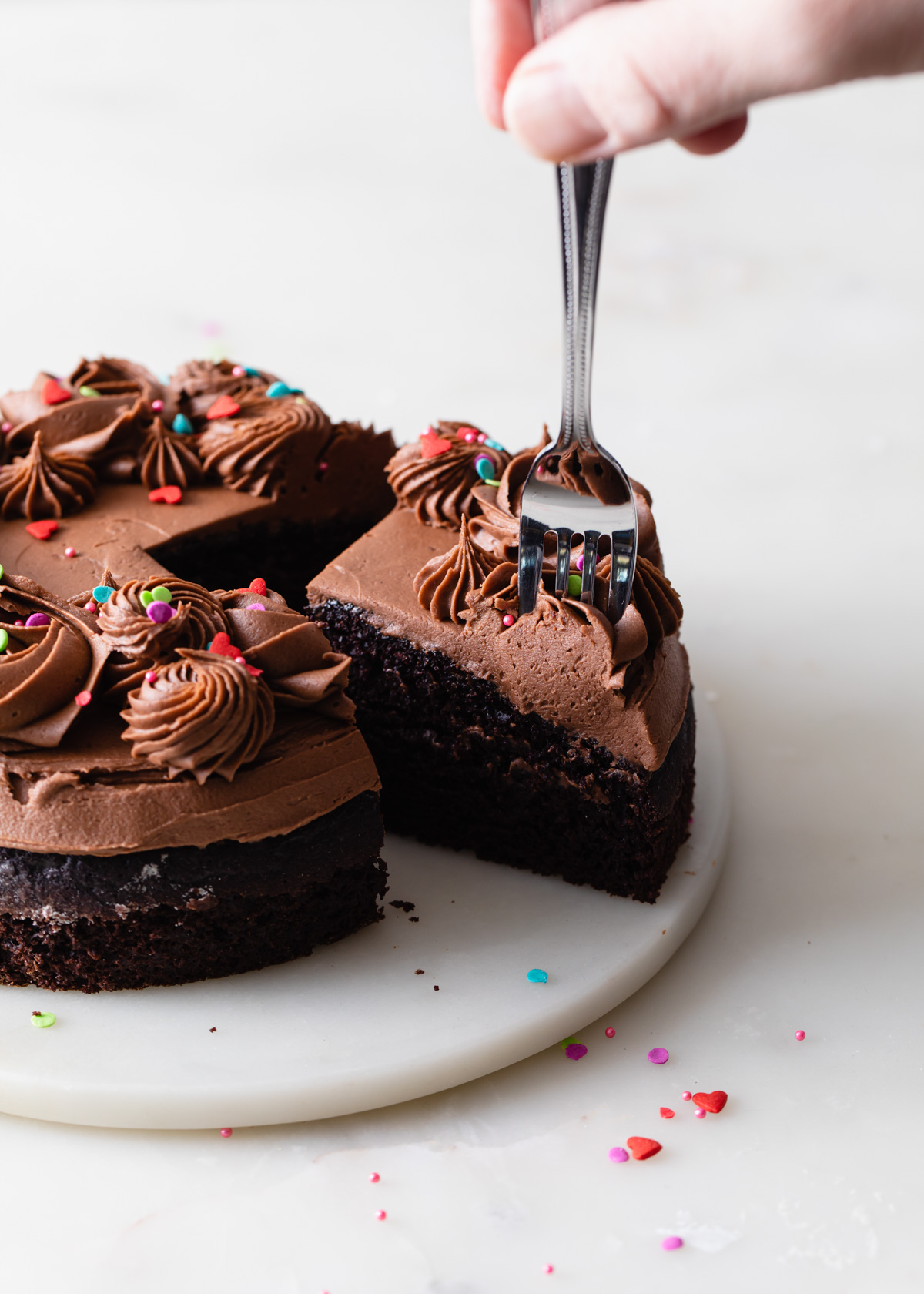 A slice of mini chocolate cake for two with fudge frosting and sprinkles being eaten with a fork