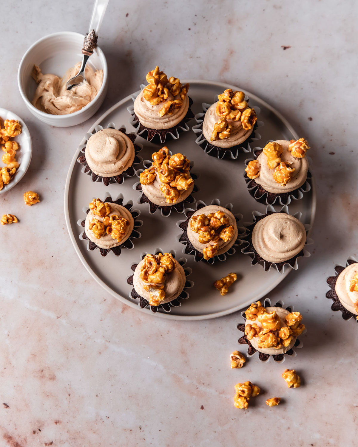 A platter of chocolate cupcakes with swirls of peanut butter frosting on top and caramel popcorn