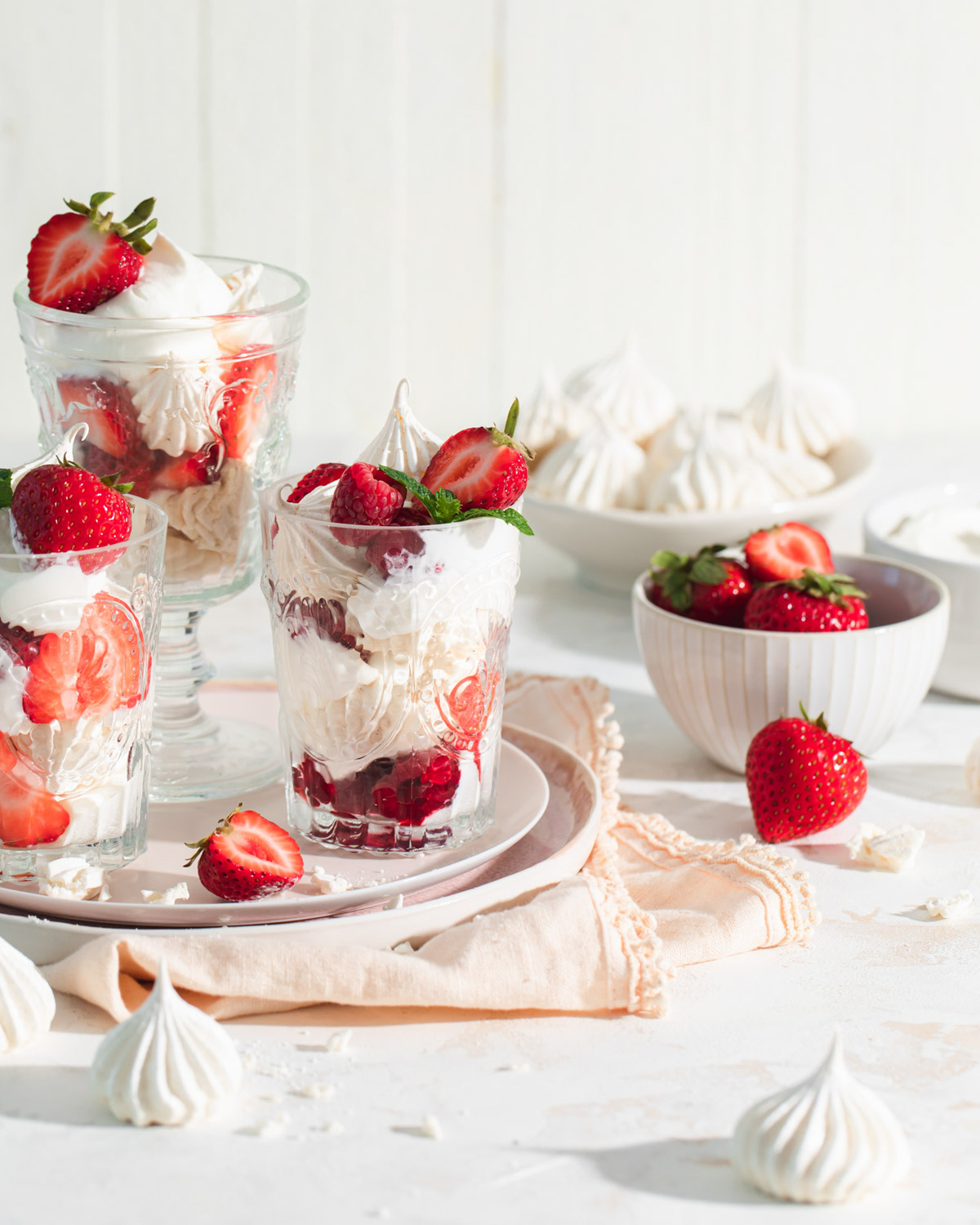 Small glasses with layers of crushed meringue, whipped cream, and fresh berries inside