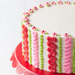A white layer cake with pink, red, and green piping