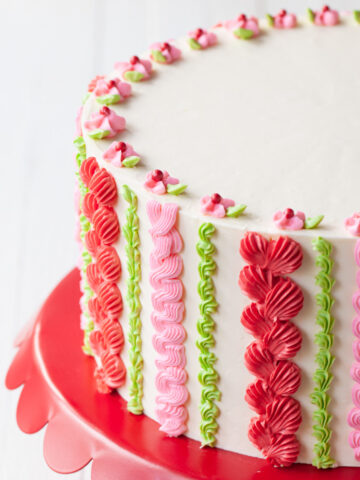 A white layer cake with pink, red, and green piping