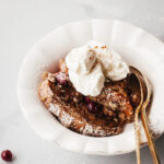 A bowl of baked gingerbread French toast with whipped cream and cranberries