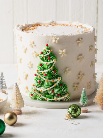 A white buttercream cake with a piped Christmas tree on the front