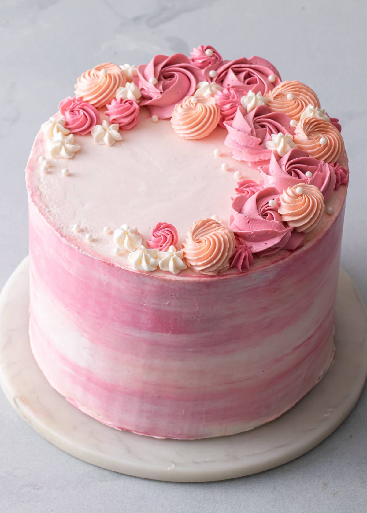 A pink and peach watercolor buttercream cake with piped flowers on top