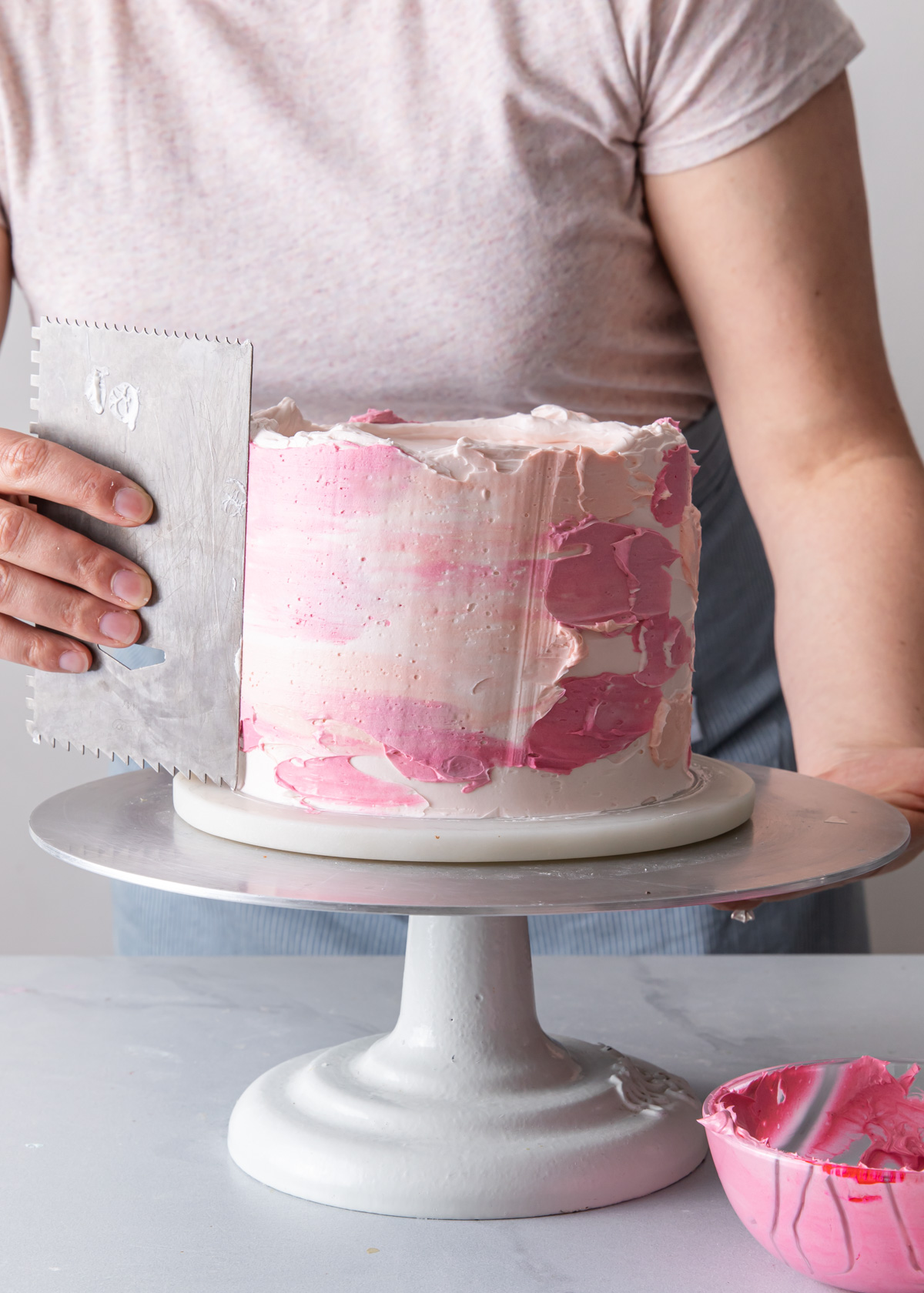 Smoothing out the frosting on a pink watercolor buttercream cake
