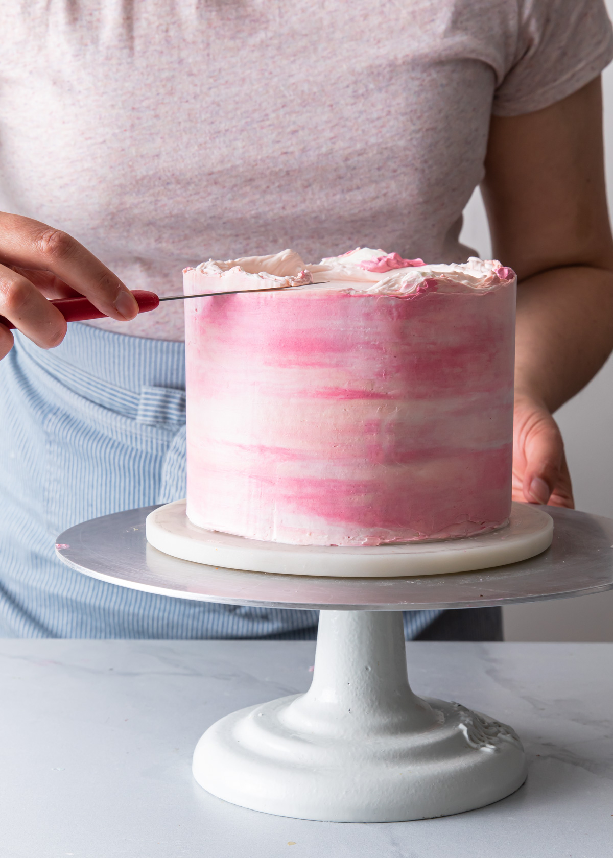 Trimming the top edge of a buttercream cake with a paring knife