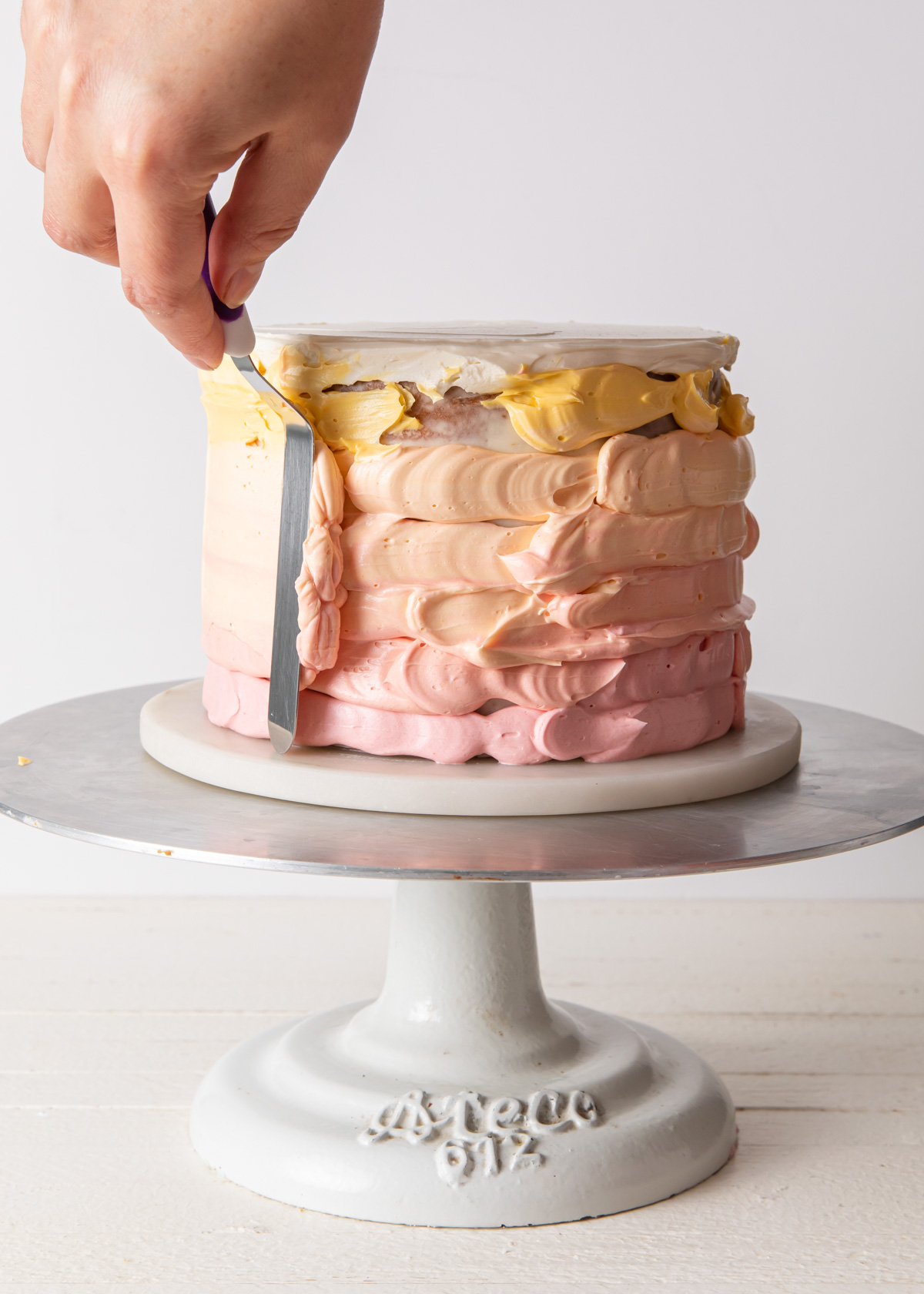 Spreading the buttercream on an ombre cake with an offset spatula