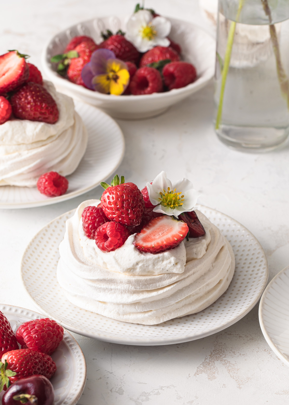 A close-up image of a mini pavlova nest that's been filled with whipped cream and fresh summer berries.
