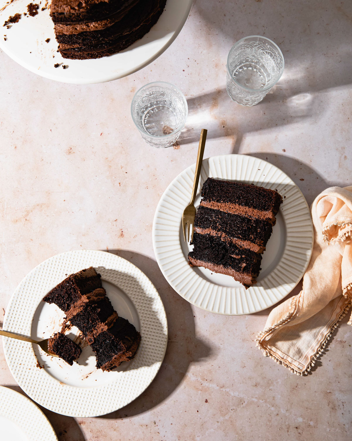 An overhead image of a couple slices of chocolate cake on white plates with harsh shadows.