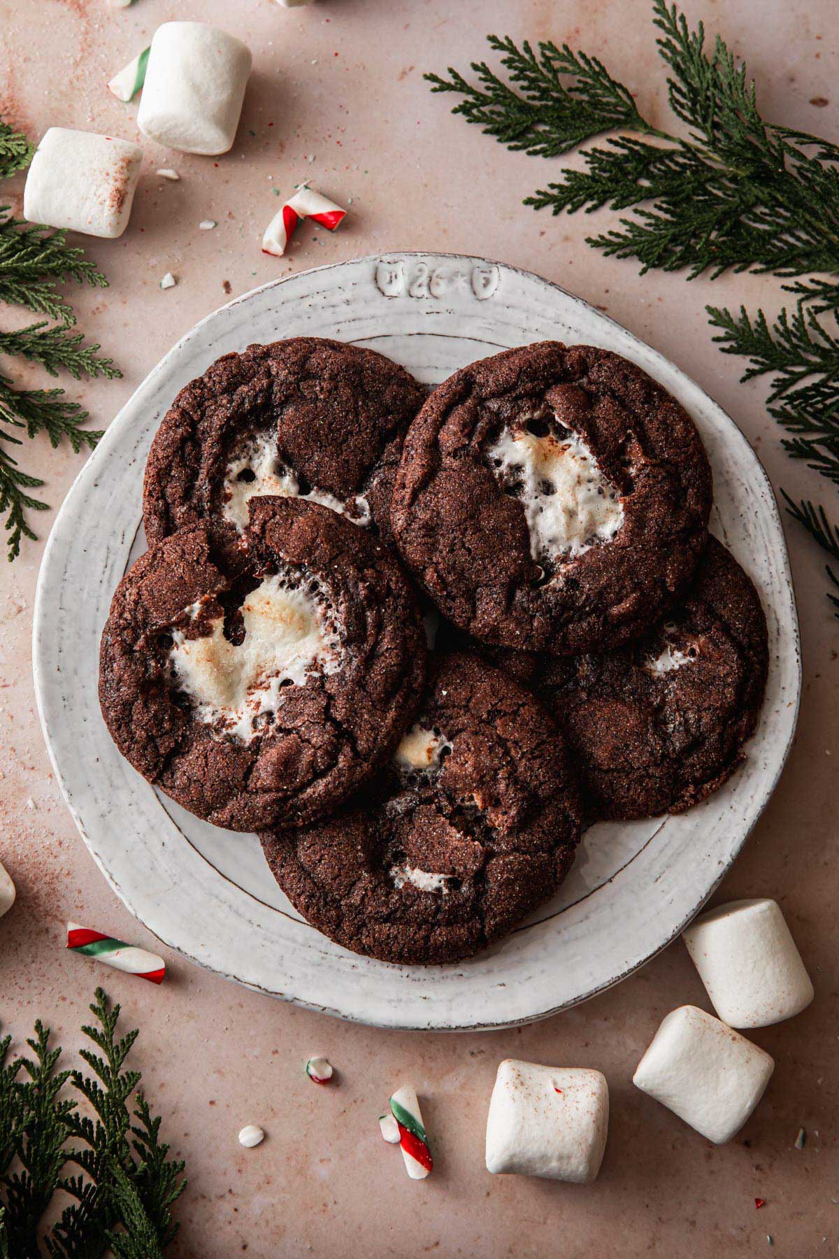 A plate of peppermint hot chocolate cookies with marshmallows and candy cane sprinkled in the background