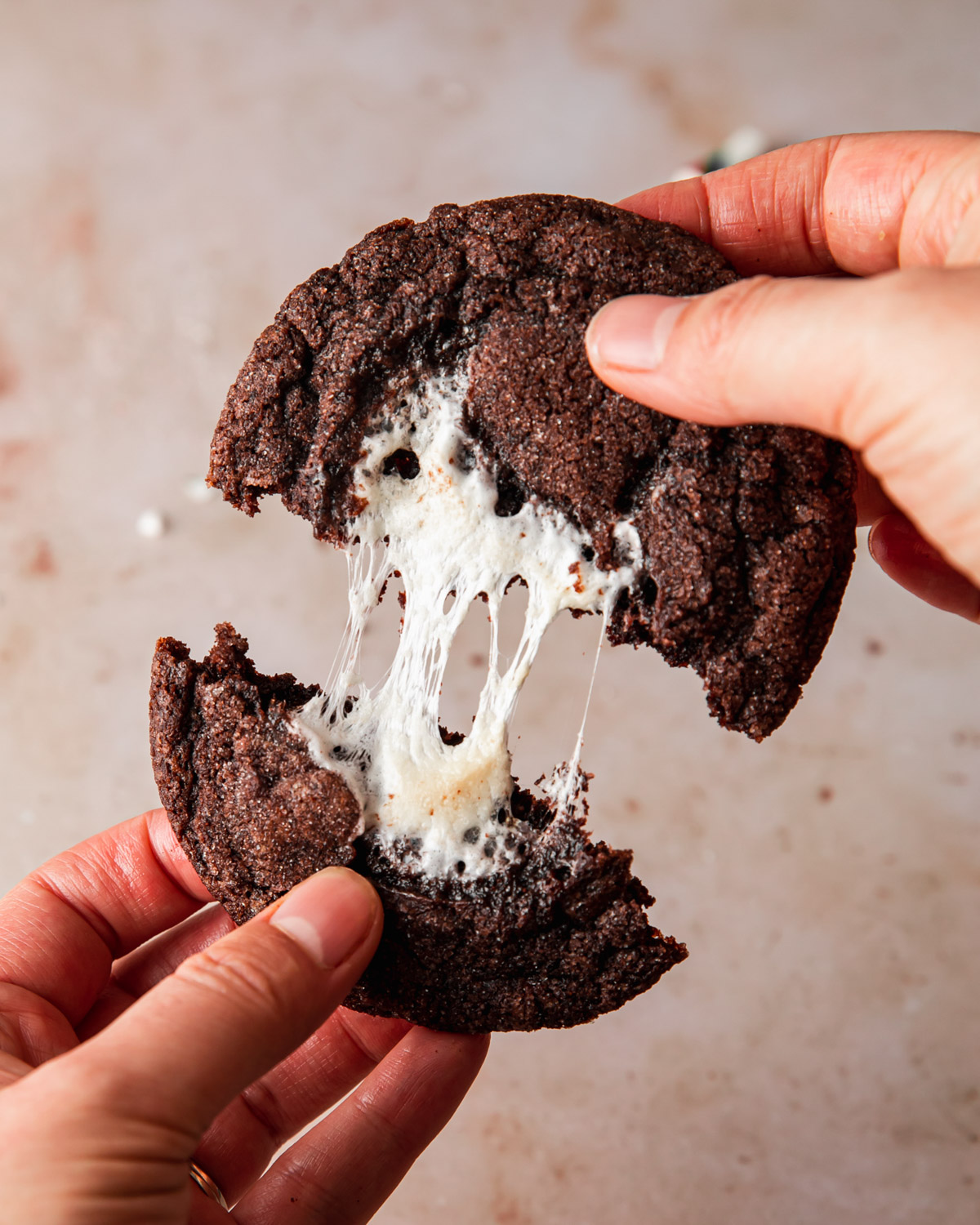 A hot chocolate cookie being pulled apart with gooey marshmallow in the center
