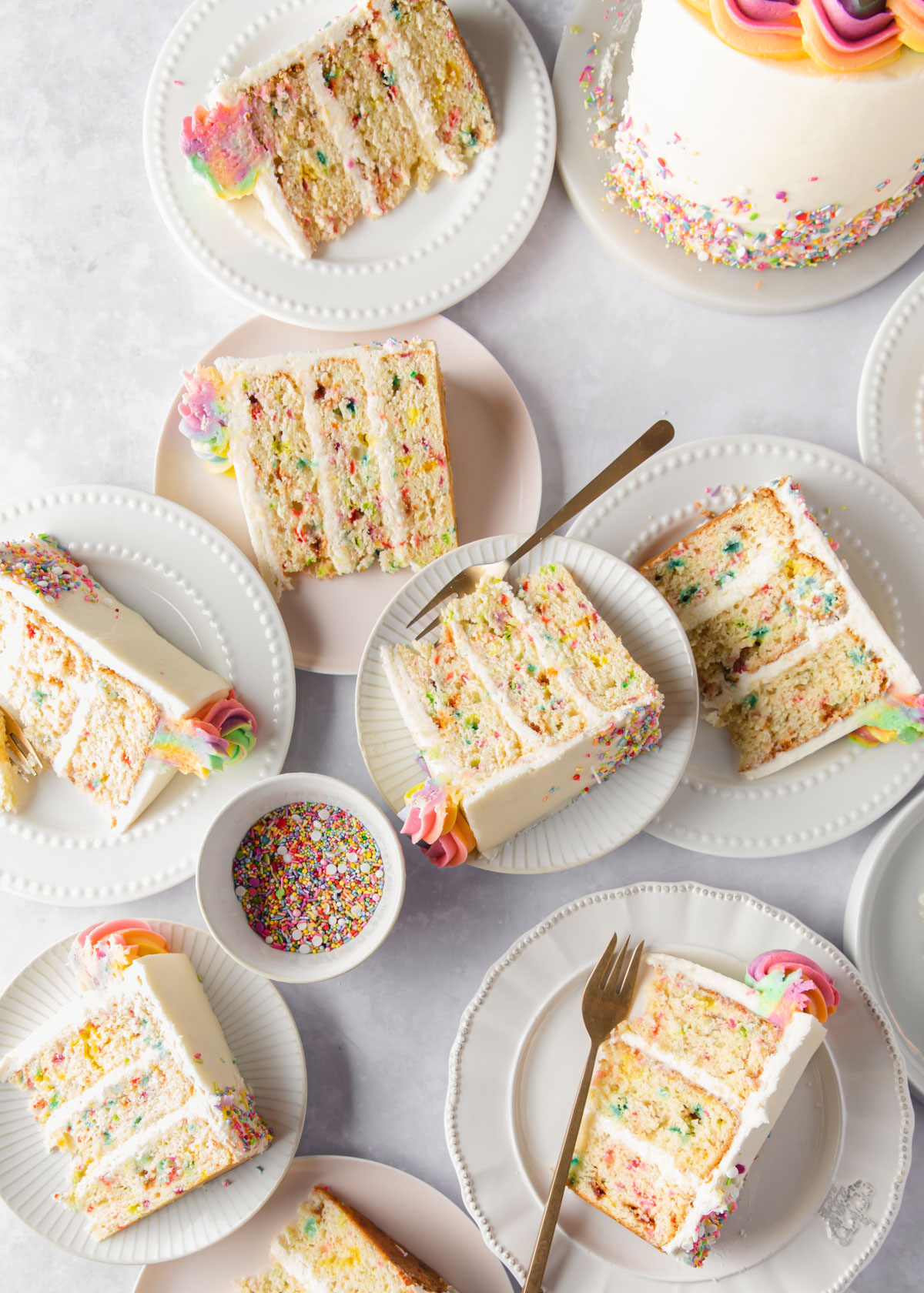 An overhead image of multiple slices of rainbow sprinkle cake