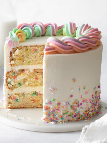 A three-layer sprinkle cake with vanilla buttercream and rainbow buttercream piped border